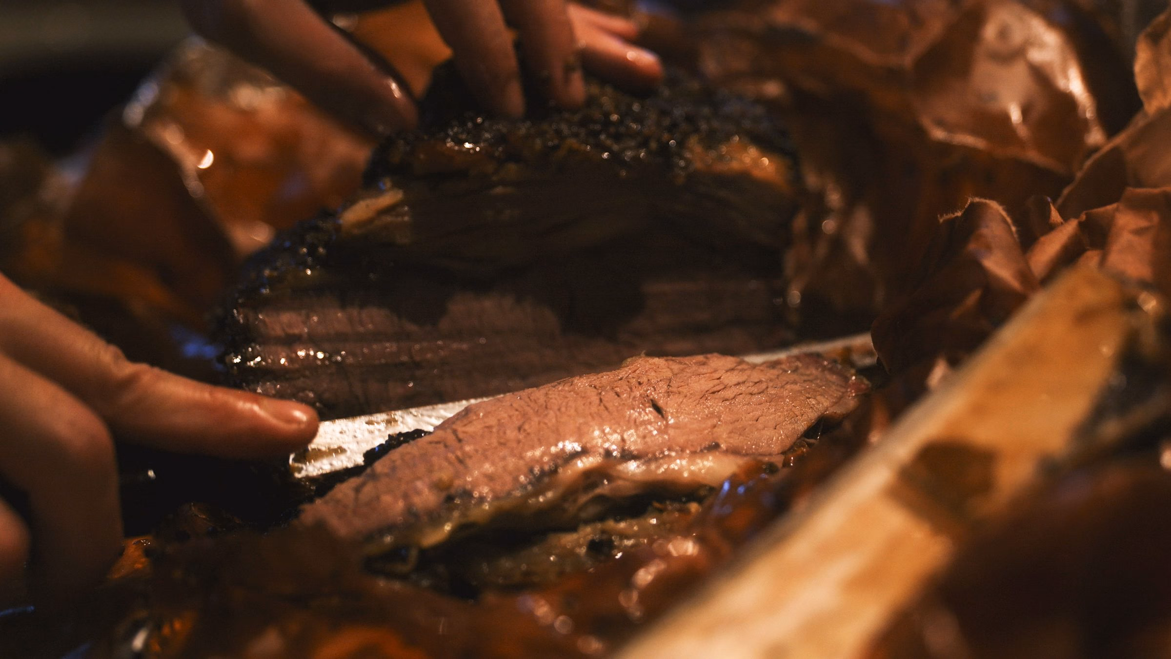 Découpe d’un brisket fumé au bark sombre sur une planche en bois