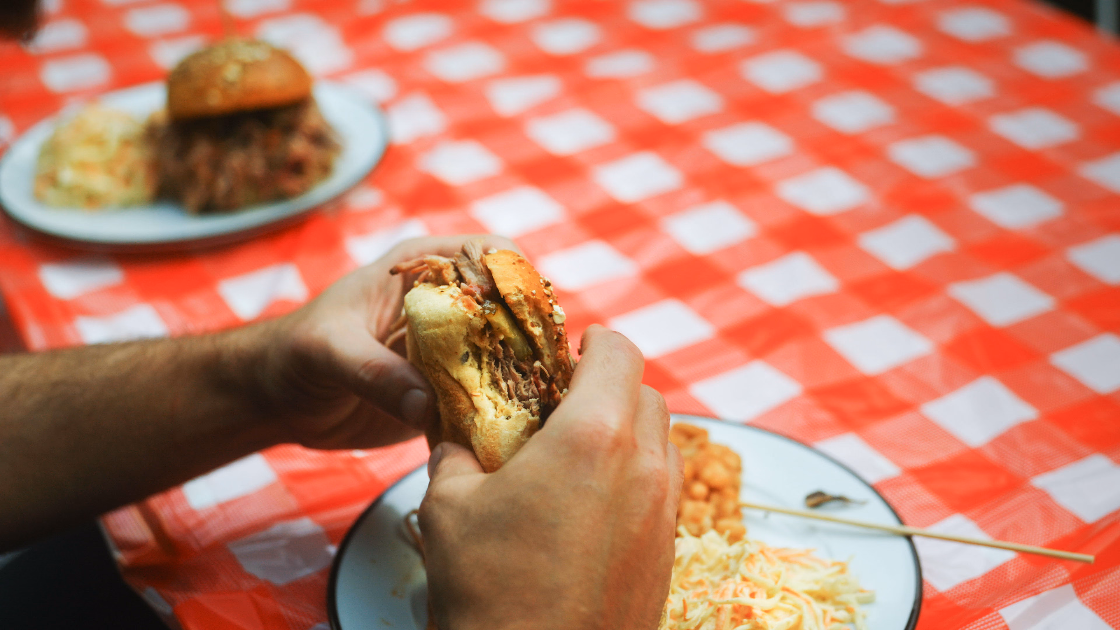 Burger fumé tenu à deux mains au-dessus d’une nappe vichy